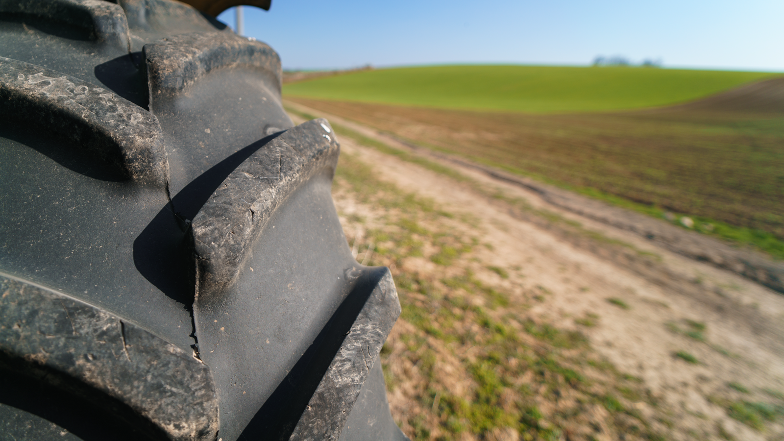 Close-up of a large lugged agricultural tractor tire beside a farm field and dirt access road