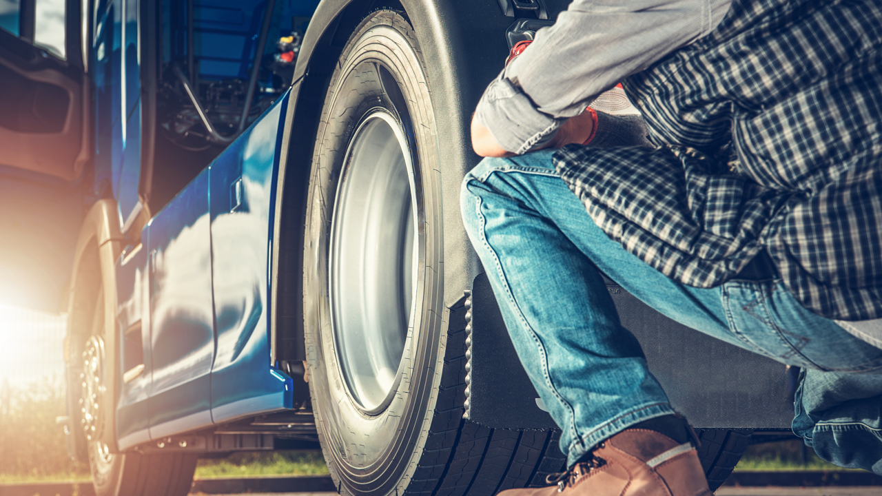 A technician kneels to inspect a commercial truck tire during a roadside inspection