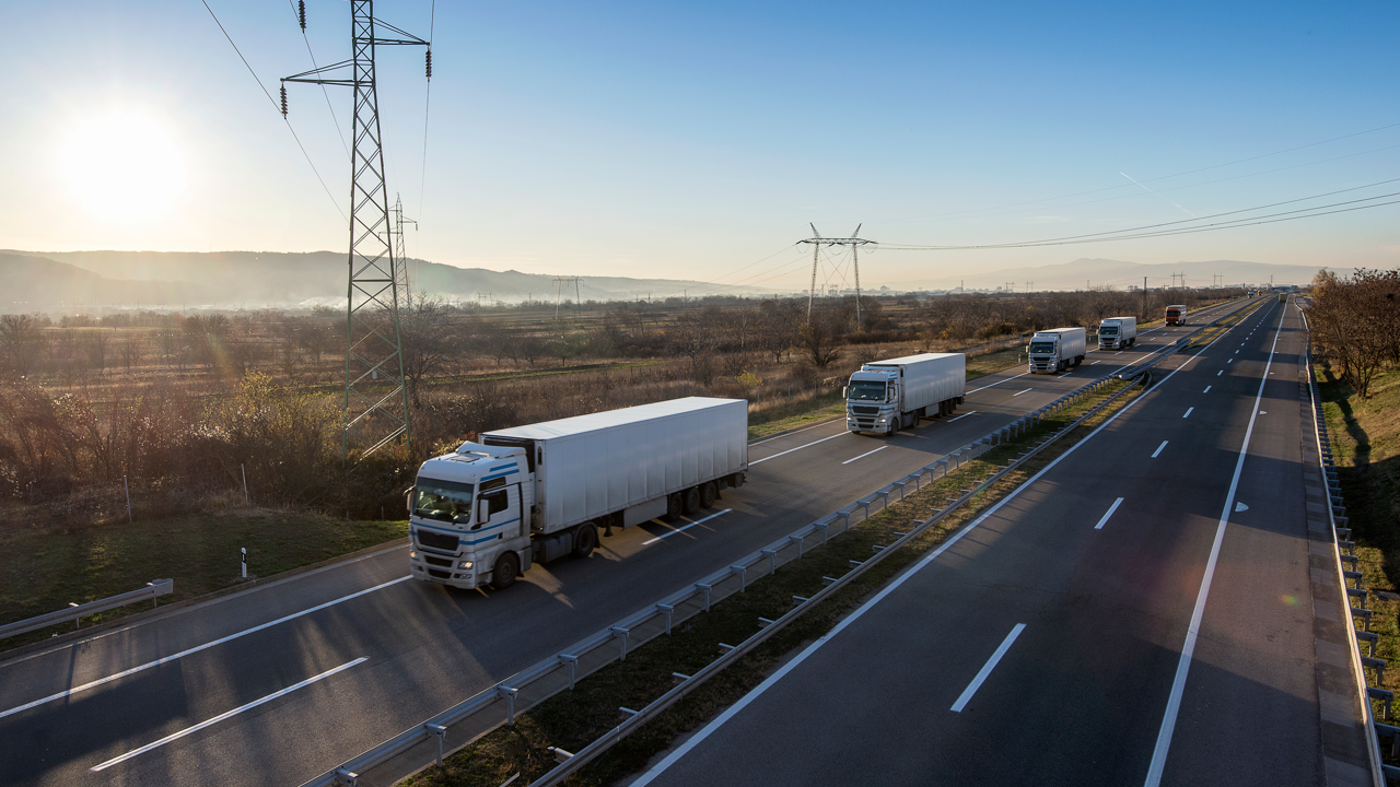 Fleet of commercial trucks on a highway — most fleets access retreading through a single external network's capacity and pricing