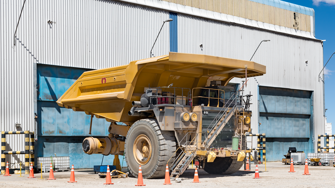 A mining haul truck at a maintenance workshop with one giant OTR tire removed for service, cordoned off with safety cones