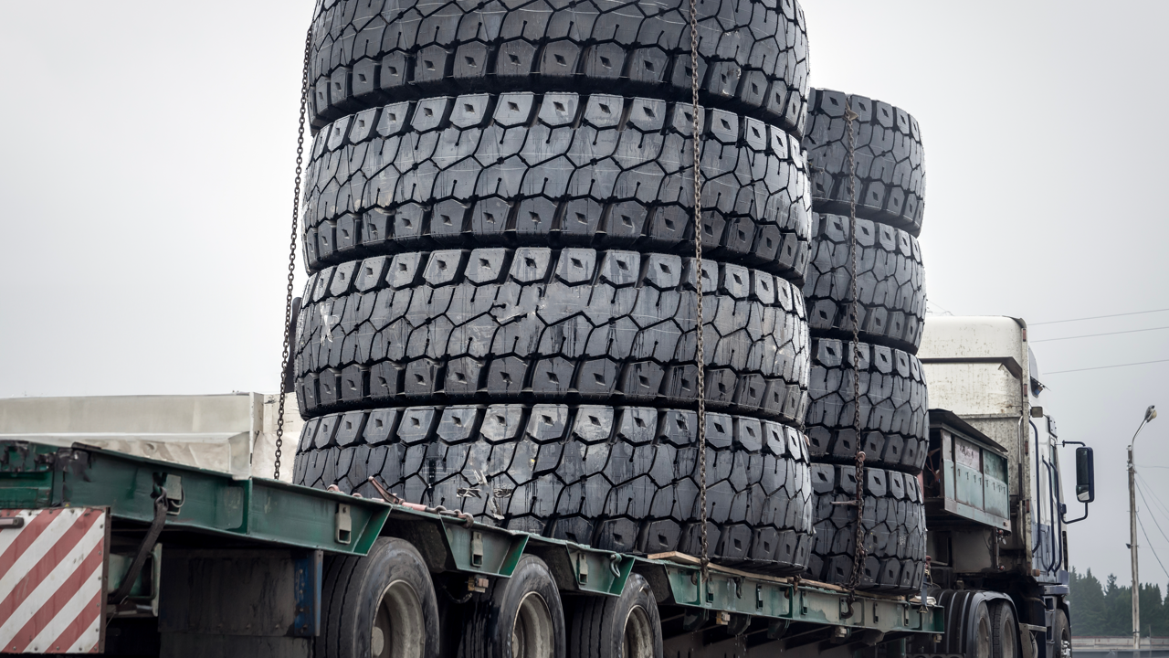 A set of huge heavy-duty truck tires chained to a flatbed trailer — the retread supply chain the U.S. industry runs on in 2026
