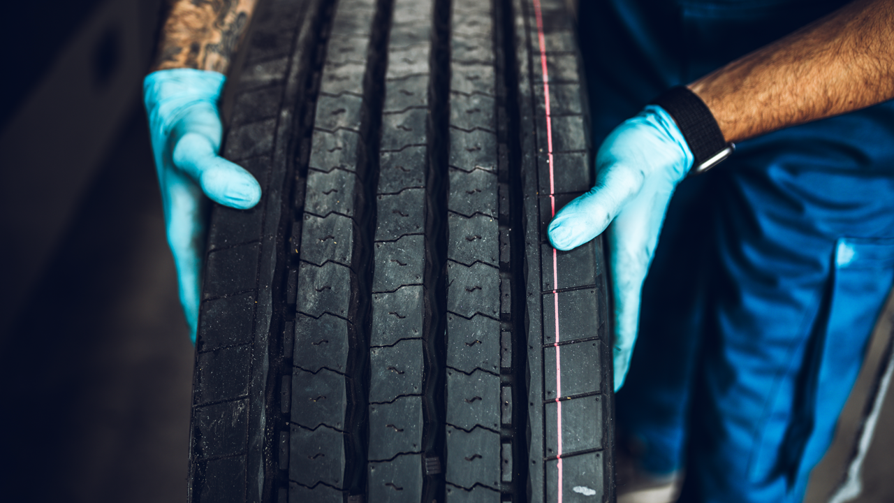 Technician inspecting a commercial bus tire — transit and municipal fleets retread for budget and duty-cycle reasons specific to public service