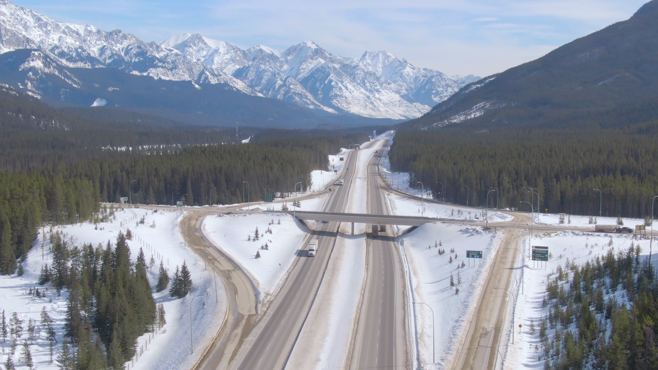 Aerial view of a highway through snow-covered mountains with trucks hauling freight — Canadian fleets running mountain or Quebec routes face very different winter tire rules depending on the province